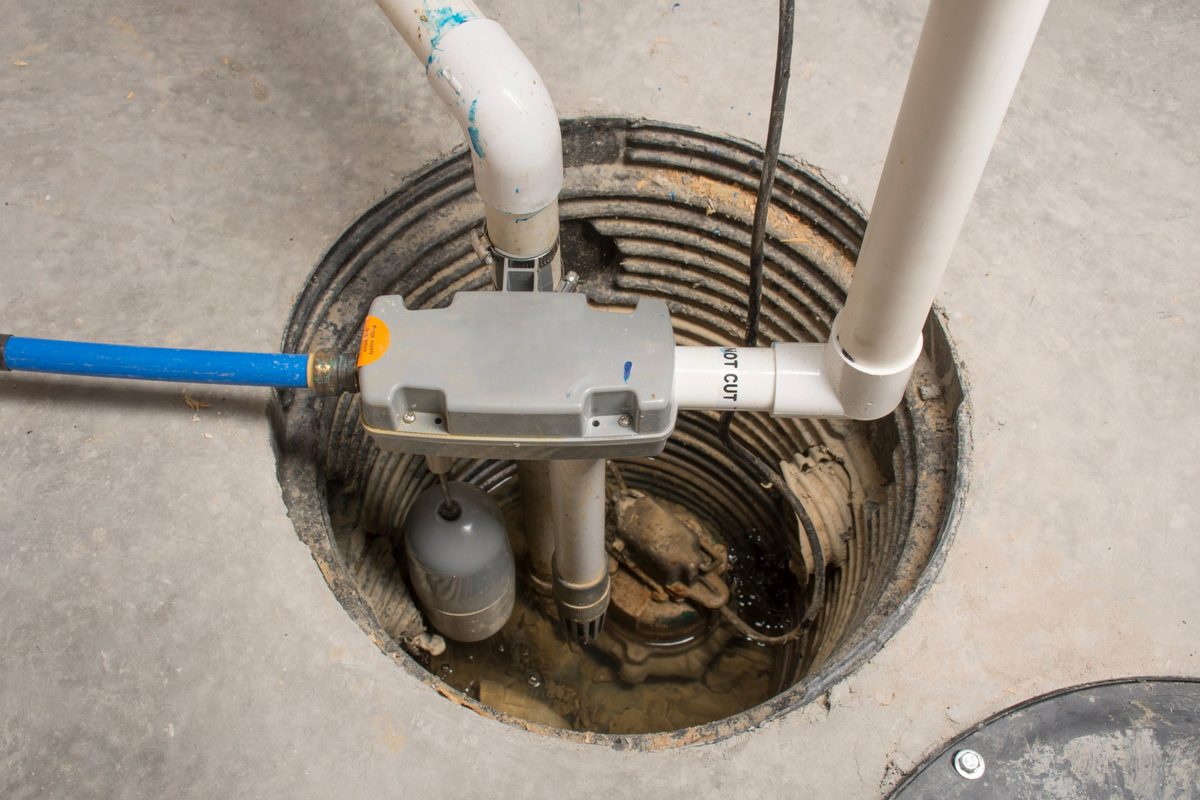 Sump pump in a basement pit with its float switch, check valve and white PVC discharge pipe