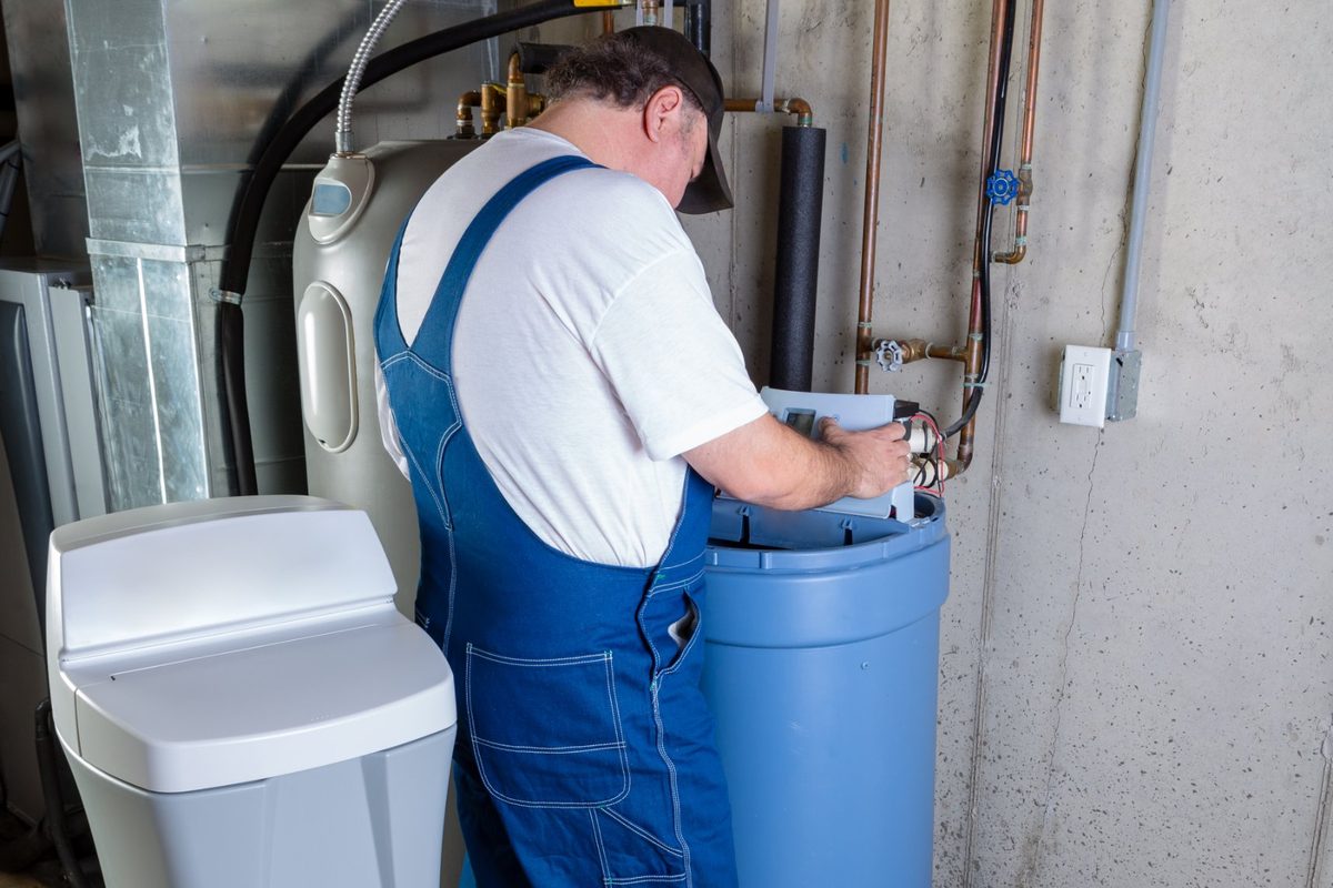 Plumber servicing the control valve on a water softener in a basement utility room